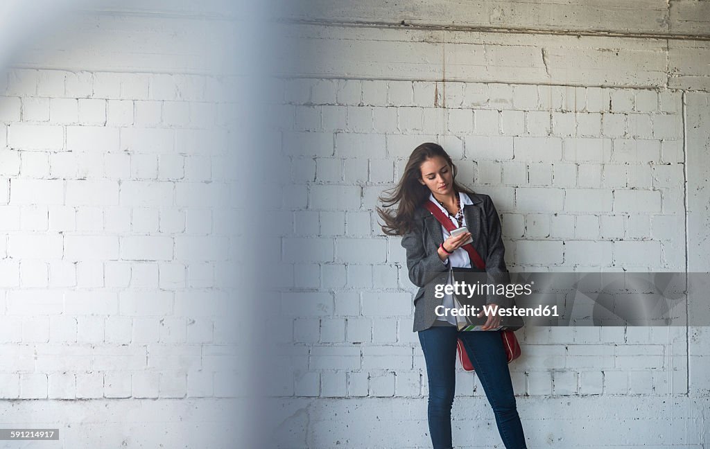 Young woman holding folder and looking at cell phone