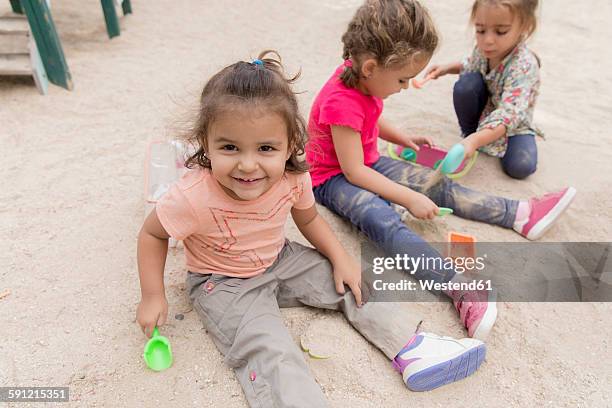 three little girls playing in the sandbox of a playground - sandkasten stock-fotos und bilder