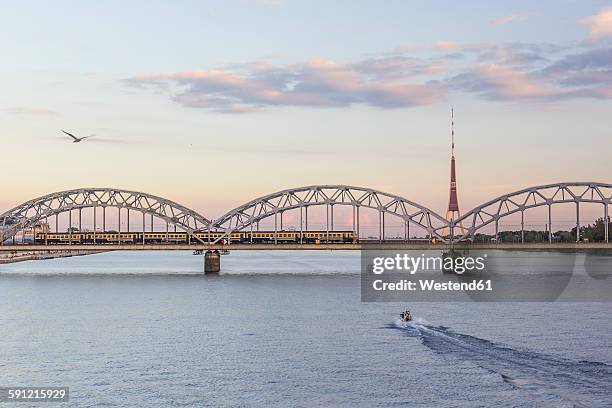 latvia, riga, railway bridge and tv tower at the daugava river in the evening - riga stock-fotos und bilder