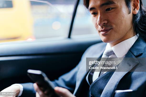 smiling businessman on back seat of car using cell phone - management car smartphone stock-fotos und bilder