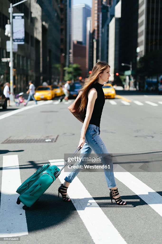 USA, New York City, young woman with rolling suitcase crossing a street