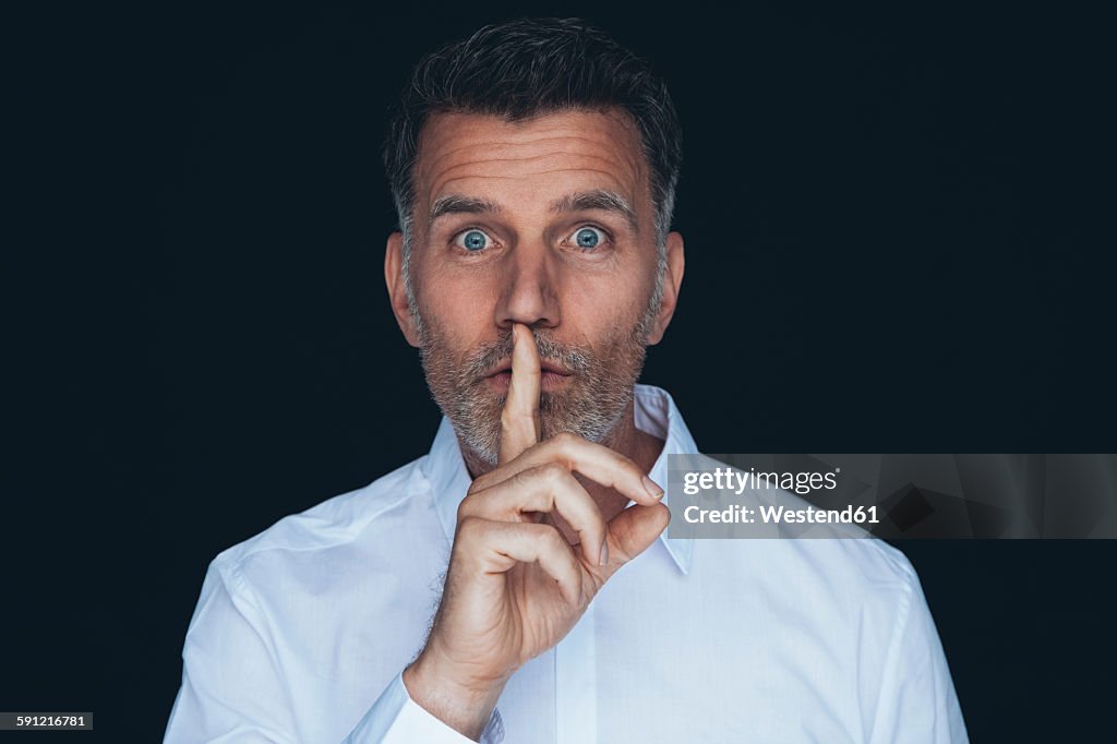 Portrait of man with finger on his mouth in front of black background