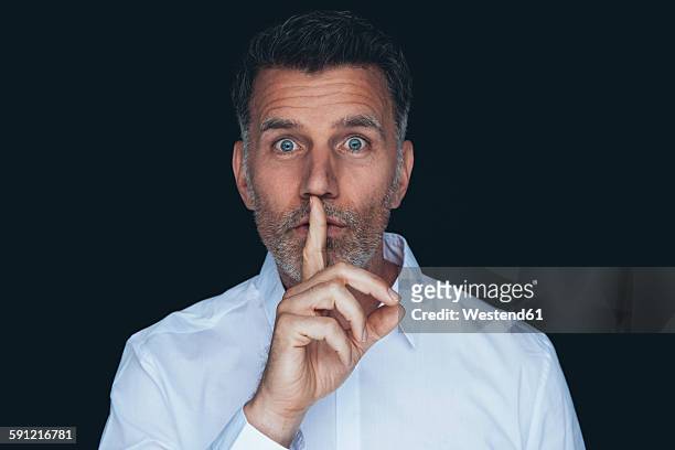 portrait of man with finger on his mouth in front of black background - shh stock pictures, royalty-free photos & images