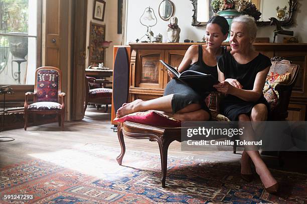two fashionable women looking at photograph book - rich man stock-fotos und bilder