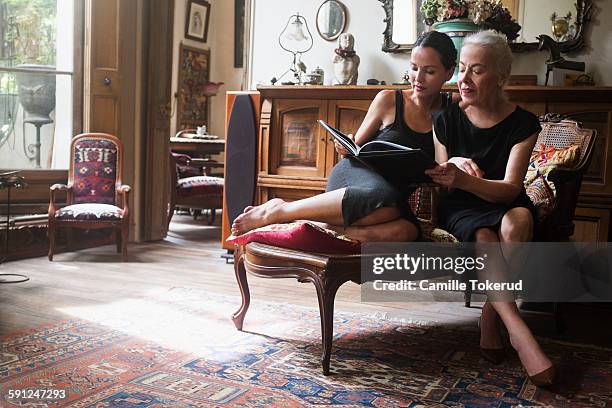 two fashionable women looking at photograph book - richesse photos et images de collection