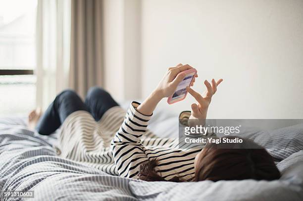woman using the smartphone on bed - アクセス ストックフォトと画像