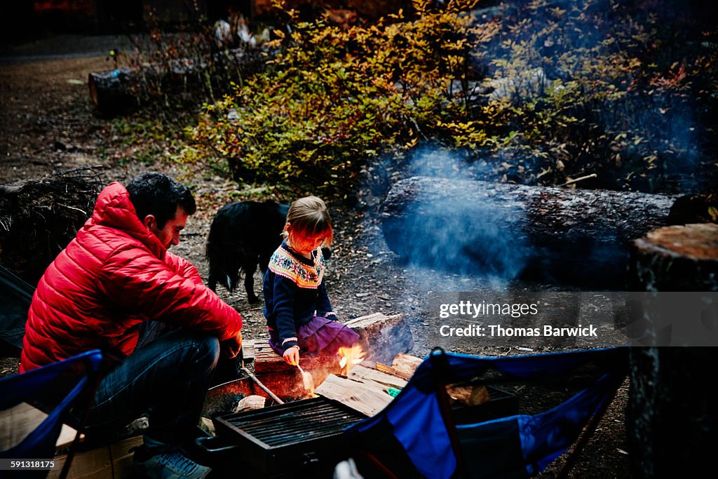 Girl sitting with father near fire while camping