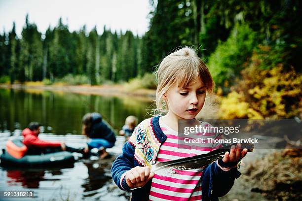 Girl standing on shoreline of lake holding feather