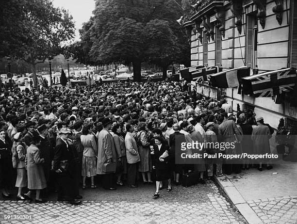 Crowds of people stand on the street outside a building to watch television broadcast of the Coronation of Queen Elizabeth II on a series of...