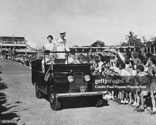 Queen Elizabeth II and Prince Philip, Duke of Edinburgh wave from the back of an open Land Rover as they drive past long lines of children during a...