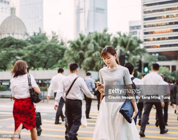 young lady using smartphone while crossing road - persona in secondo piano foto e immagini stock