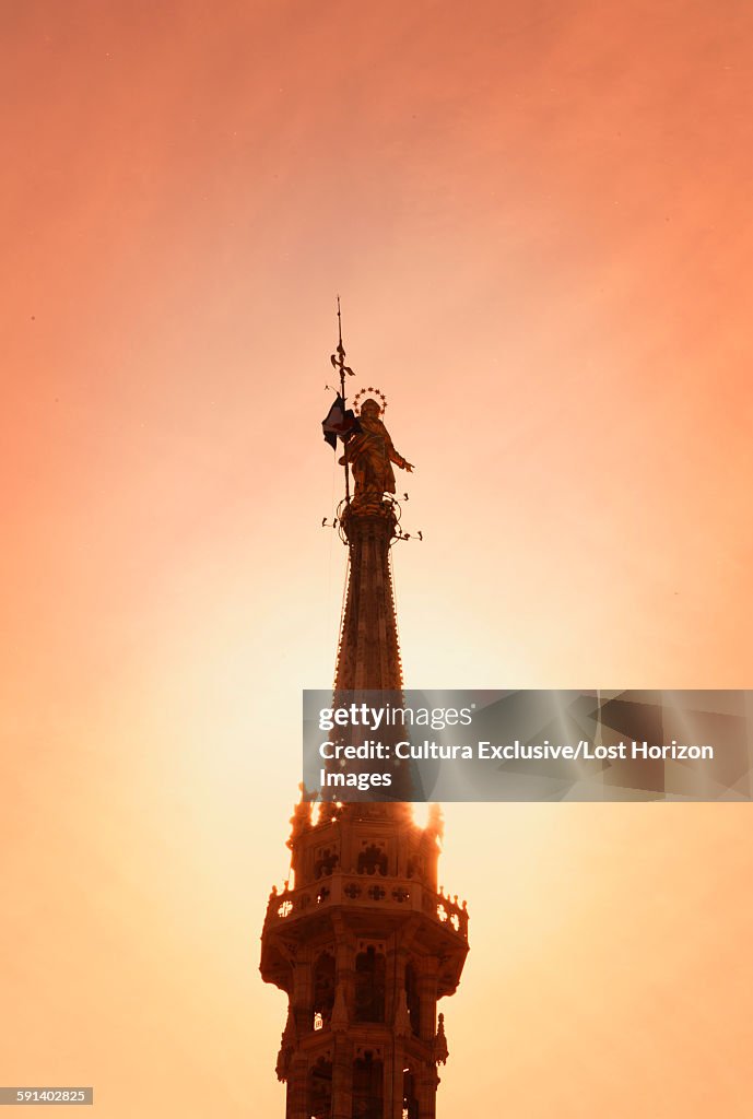 Sunlit silhouetted statue of the Madonna (la Madonnina) on the highest spire of the Milan Cathedral, Italy