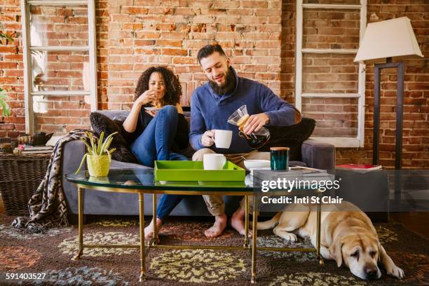 couple enjoying breakfast on sofa in living room - mann frau hund zuhause stock-fotos und bilder