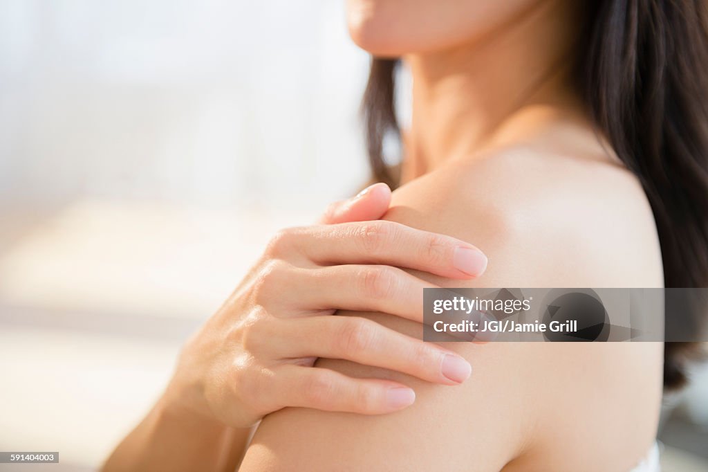 Mixed race woman rubbing lotion into skin