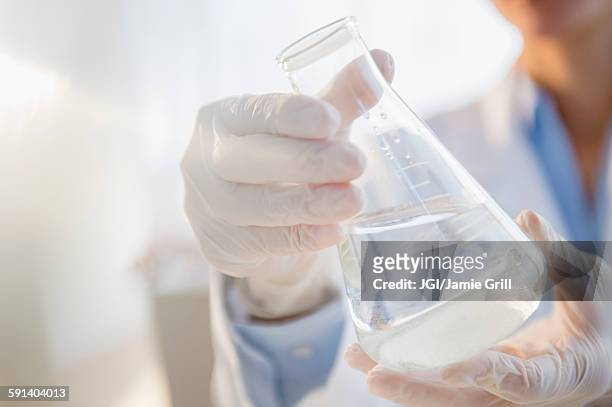 mixed race scientist examining beaker in laboratory - ビーカー ストックフォトと画像