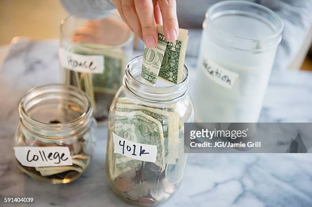 mixed race woman saving money in jars - frugalidad fotograf�ías e imágenes de stock