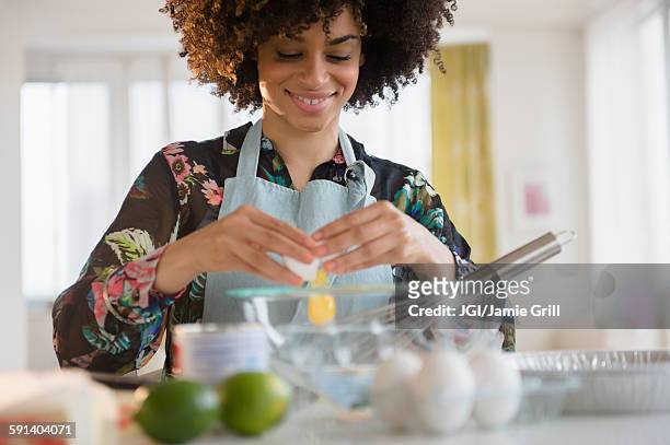mixed race woman cracking egg - woman baking stock-fotos und bilder