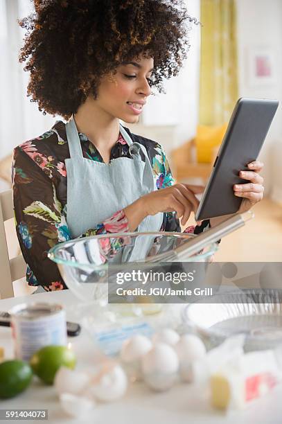 mixed race woman baking with recipe on digital tablet - baking reading recipe stockfoto's en -beelden