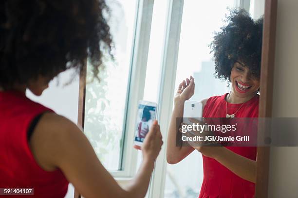 mixed race woman taking selfie with cell phone in mirror - mirror selfie - fotografias e filmes do acervo