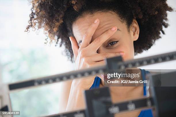 mixed race woman hiding from weight on scale - preocupación por el cuerpo fotografías e imágenes de stock