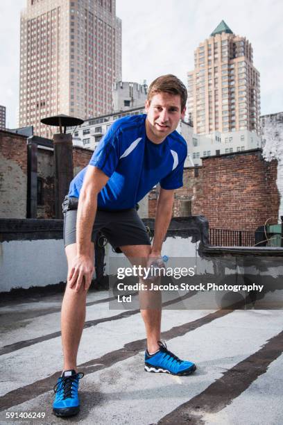 caucasian athlete resting on urban rooftop - buigen-lichaamsbeweging stockfoto's en -beelden
