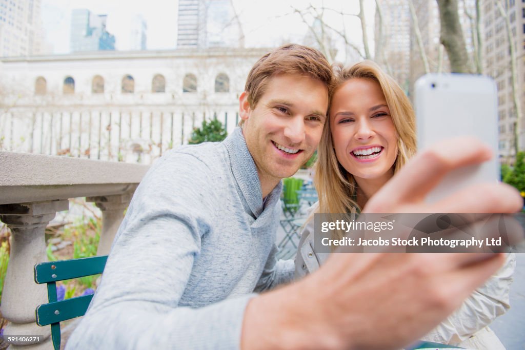 Caucasian couple taking selfie with cell phone in city