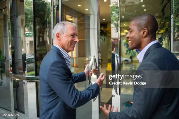 businessman opening office door for colleague - doors of the 21st century ストックフォトと画像