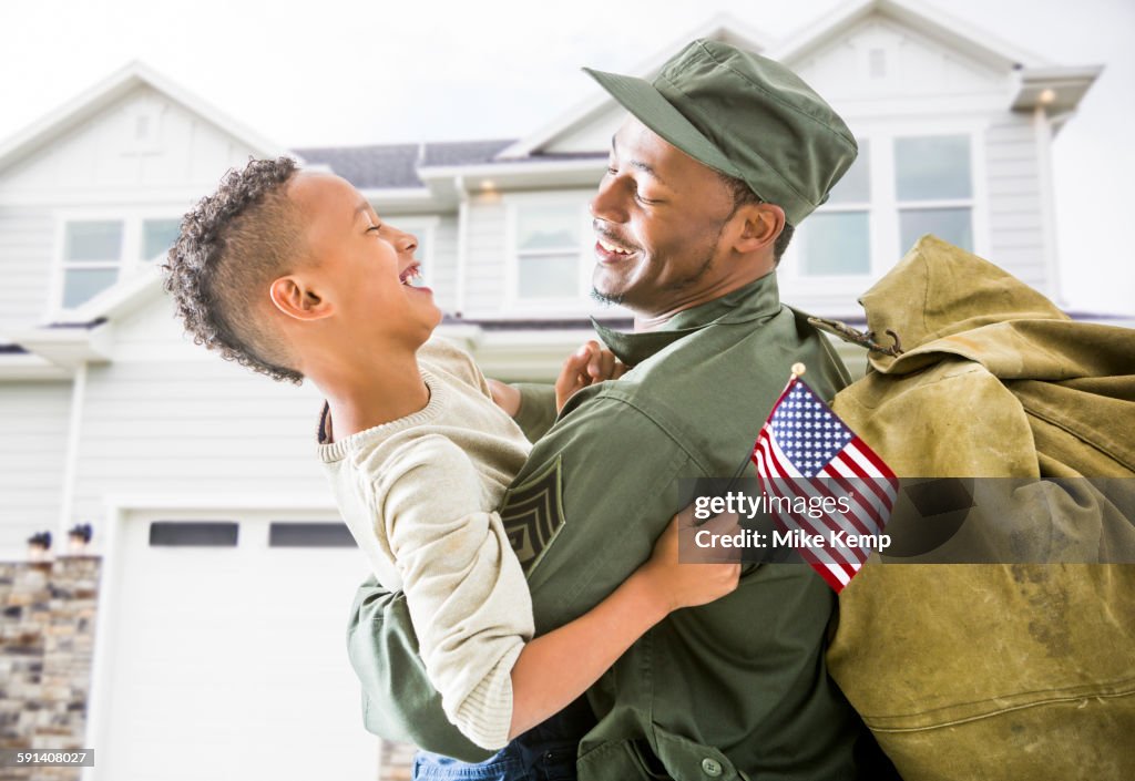 Returning soldier hugging patriotic son outside house