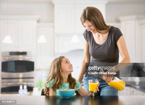 caucasian mother pouring juice for daughter in kitchen - family orange juice stockfoto's en -beelden