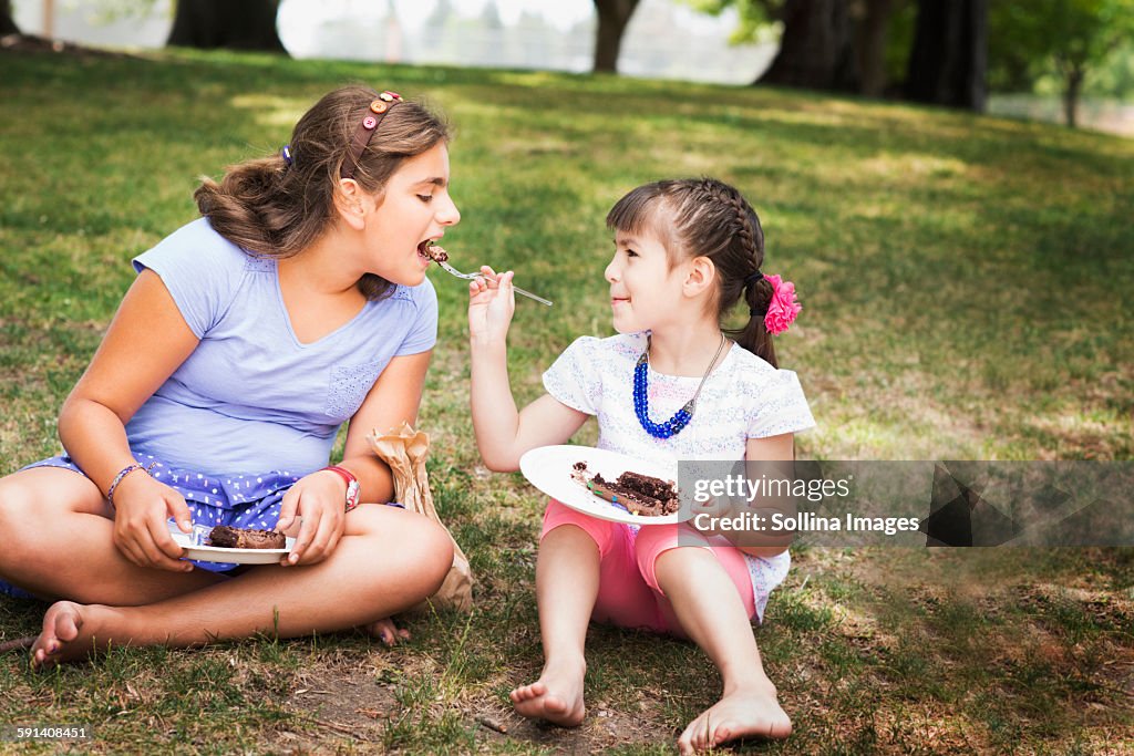 Girl feeding sister cake at birthday party in park