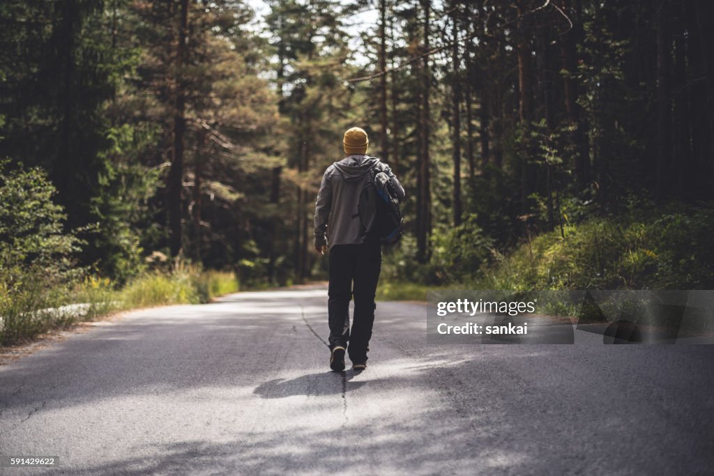 Male traveler with backpack walks forward by the road