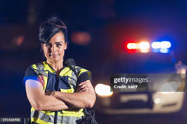 policewoman in street at night, police car in background - verkeerspolitie stockfoto's en -beelden