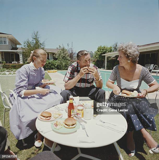 American movie producer, artist, and animator Walt Disney eats a hamburger with his wife, Lillian and one of their daughters, as they all sit at a...