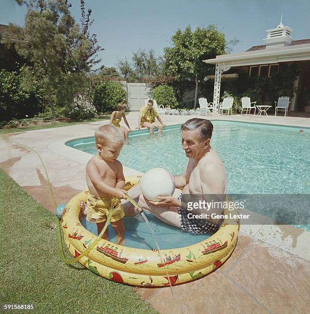 American movie producer, artist, and animator Walt Disney sits in a wading pool with one of his grandsons, 1950s.
