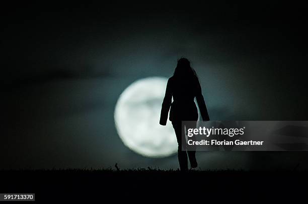 Woman walks in front of the rising full moon on December 26, 2015 in Diehsa, Germany.