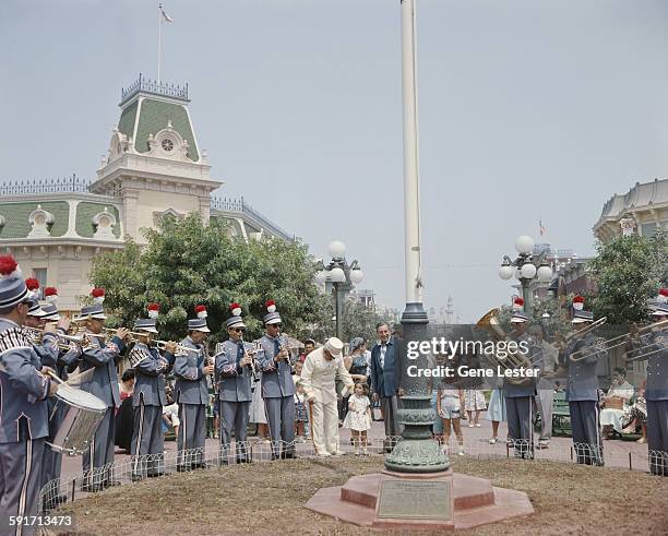 American movie producer, artist, and animator Walt Disney stands with a brass band and attendees at his Disneyland amusement park, Anaheim,...