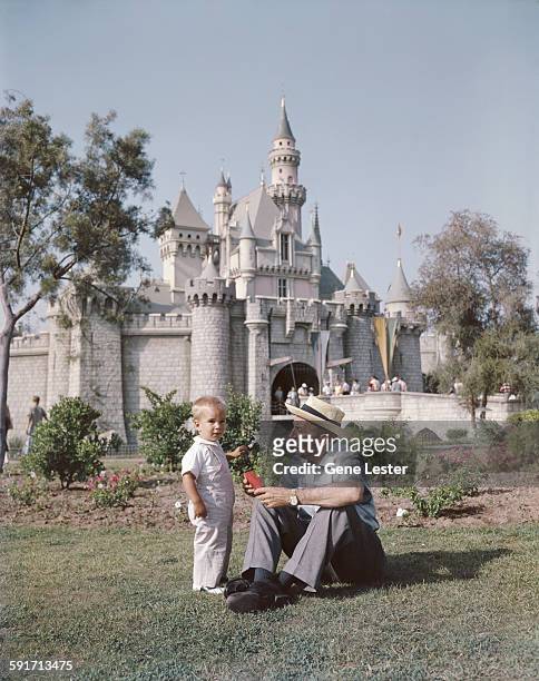 American movie producer, artist, and animator Walt Disney sits with one of his grandsons on the lawn in front of the Disneyland castle, Anaheim,...