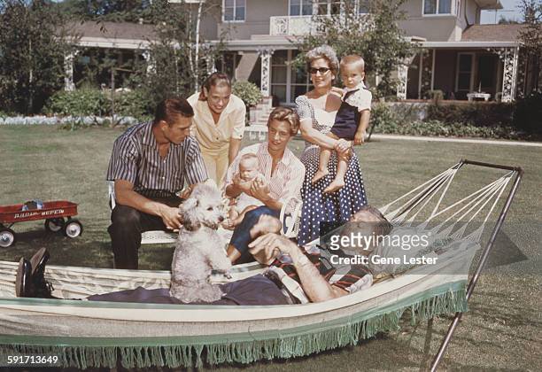 Surrounded by his family, American movie producer, artist, and animator Walt Disney lies in a hammock in the garden, with a poodle on his lap, 1950s....