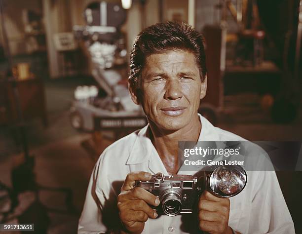 Portrait of American actor Charles Bronson as he poses on set, with a camera in his hands, circa 1958.