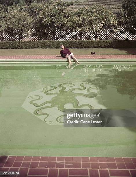 Portrait of American actor and comedian Jack Benny as he poses on the edge of his swimming pool, circa 1956. The bottom of the pool features an...