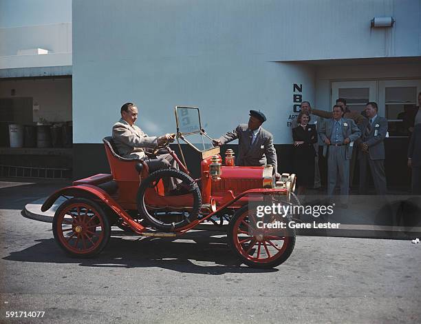 American actor and comedian Eddie 'Rochester' Anderson stands by an antique Maxwell car, as fellow comedian Jack Benny sits in the driver's seat...