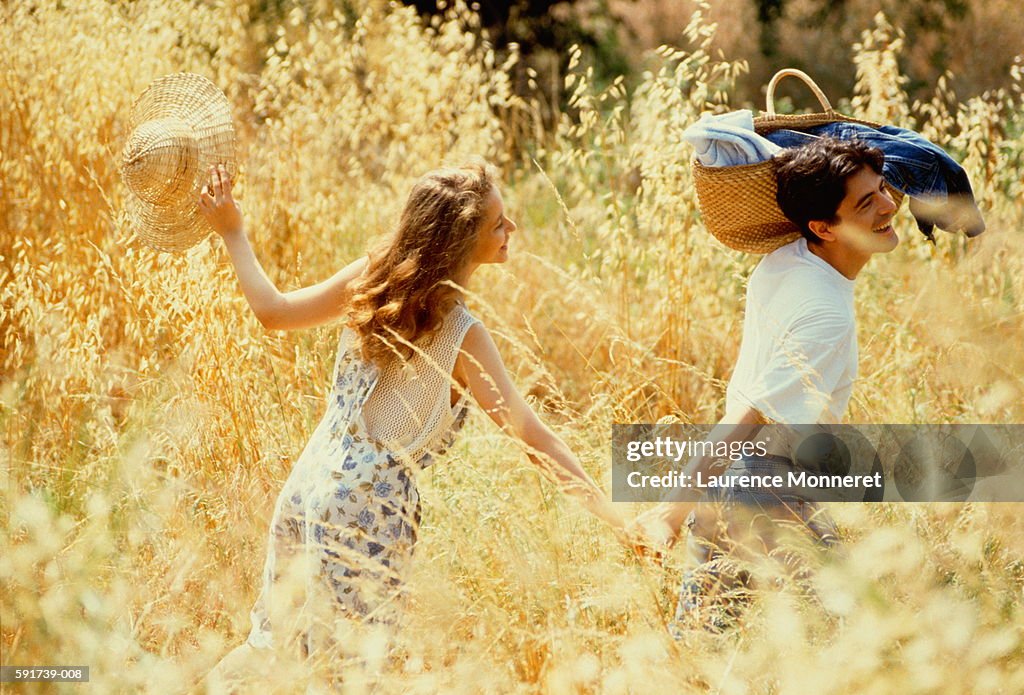 Couple walking hand in hand through field,man with basket on shoulder