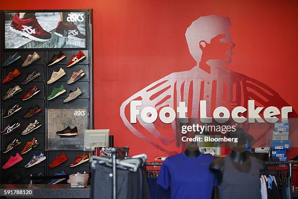 Asics Corp. Sneakers and Nike Inc. Apparel hang on display for sale in front of Foot Locker Inc. Signage inside a store on the Third Street Promenade...