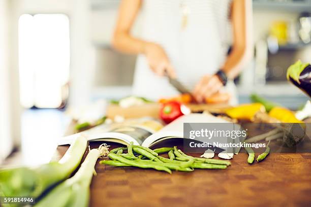 livre de cuisine et légumes sur l’îlot de cuisine avec femme en backgrou - livre de cuisine photos et images de collection