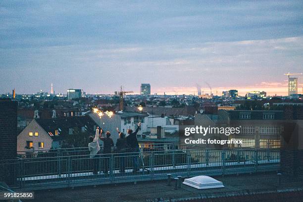 small group, young adults standing on rooftop waving sparklers,skyline - rooftop party night stock pictures, royalty-free photos & images