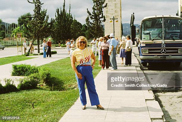 Female tourist posing for a photo, with a Mercedes Benz tour bus in the background, in front of the Monumento de La Nacion A Sus Proceres in Caracas,...