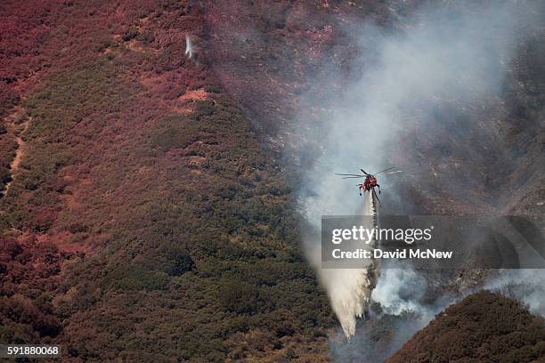 Firefighting helicopter makes a drop near a hillside painted red with fire retardant as firefighters work to protect homes along Cajon Boulevard at...