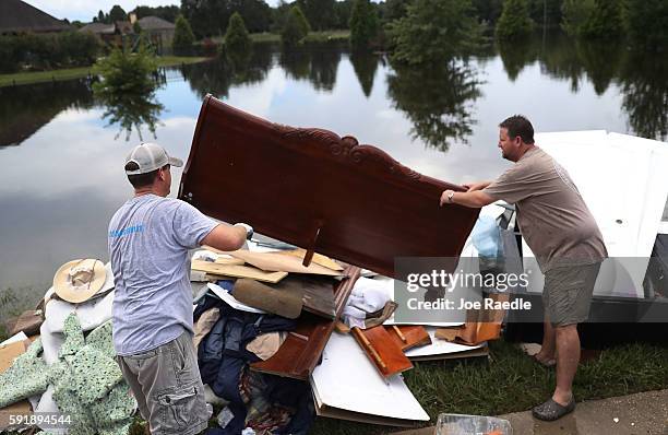 Chad Credeur helps his brother Karl Credeur toss out a headboard after it was inundated with flood water in his bedroom on August 18, 2016 in St...