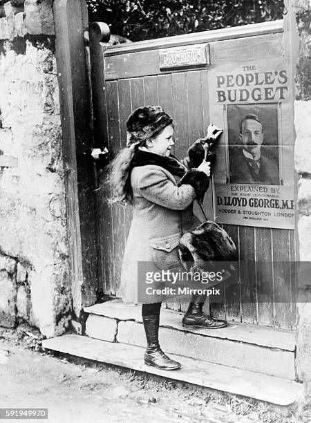 Lady Megan Lloyd George aged 8, fastens a People's Budget poster, featuring a portrait of her father David Lloyd George MP, onto the front of a gate...
