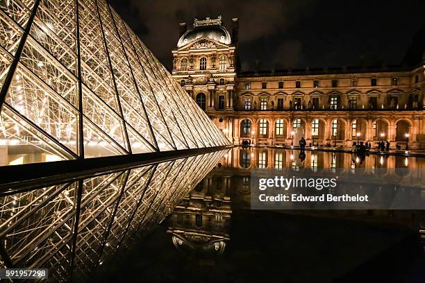 The Louvre museum, including the Louvre Pyramid made of glass and metal, reflects into a water puddle on a rainy summer day, during night time, on...